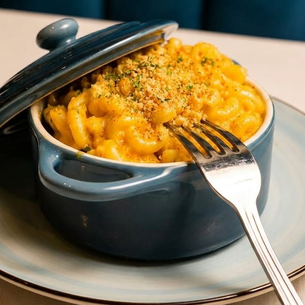Macaroni and cheese in a blue pot with a fork, topped with breadcrumbs, on a light blue plate.