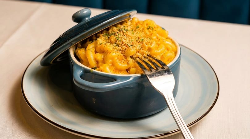 Macaroni and cheese in a blue pot with a fork, topped with breadcrumbs, on a light blue plate.