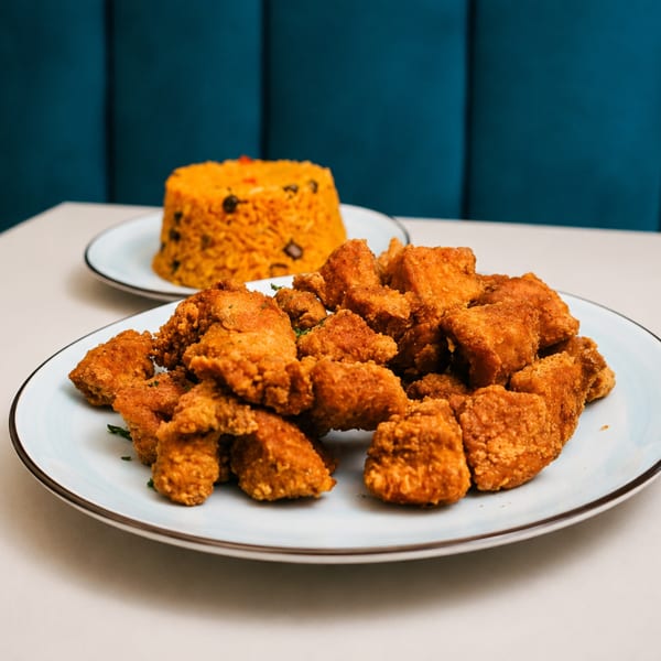 A plate of crispy fried chicken pieces with a side of yellow rice and beans.