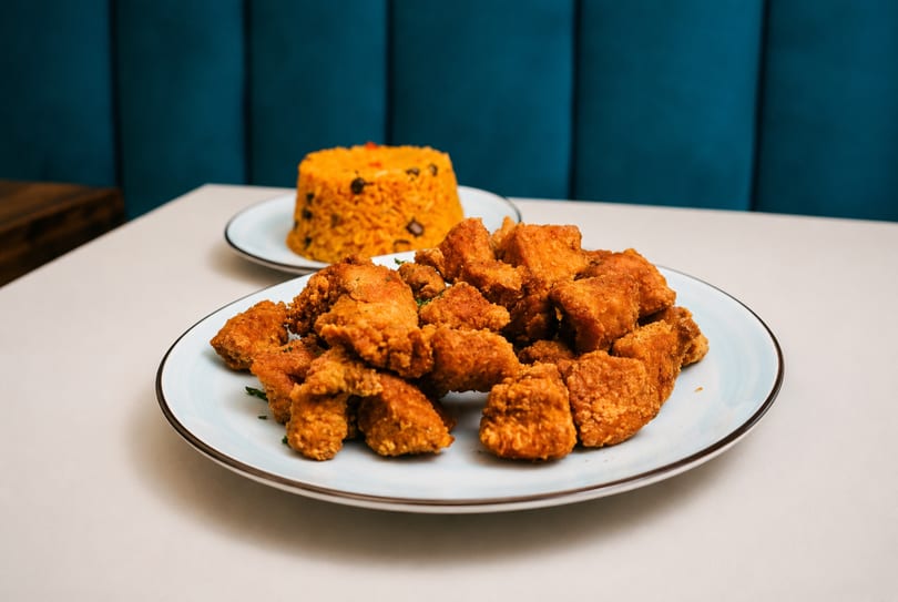 A plate of crispy fried chicken pieces with a side of yellow rice and beans.