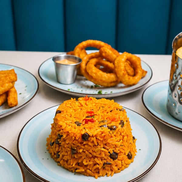Plates of yellow rice with black beans, onion rings, and fried plantains on a white tablecloth.