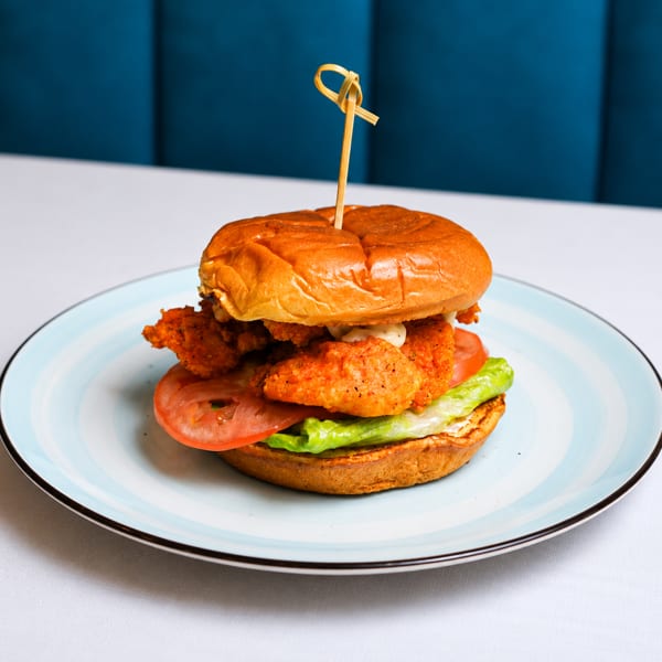 Crispy chicken sandwich with lettuce, tomato, and sauce on a brioche bun, served on a blue plate.