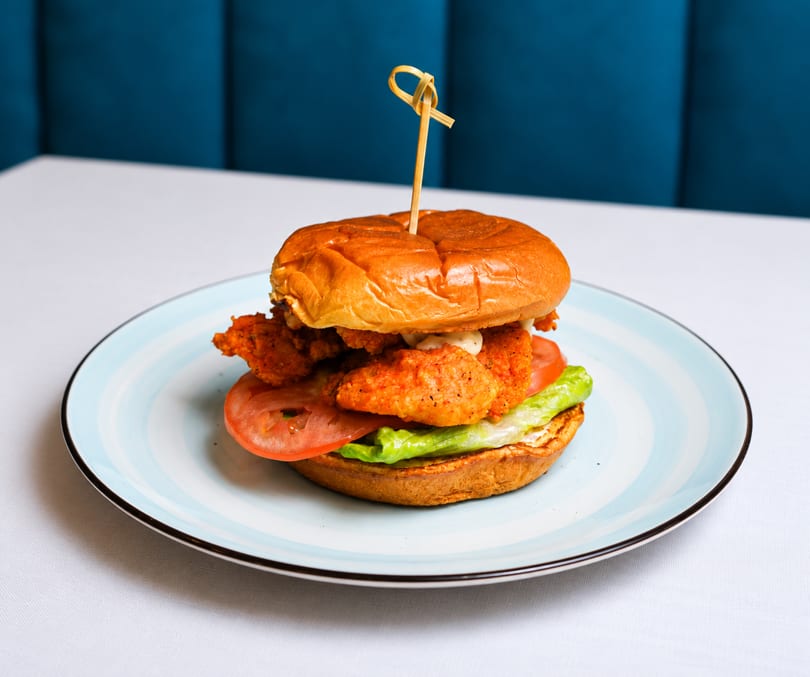 Crispy chicken sandwich with lettuce, tomato, and sauce on a brioche bun, served on a blue plate.