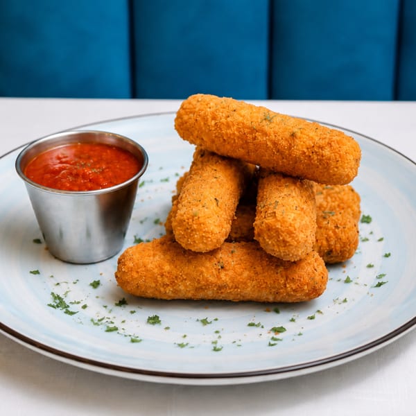 Golden-brown mozzarella sticks with a side of marinara sauce on a light blue plate.