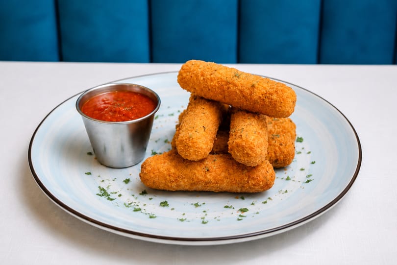Golden-brown mozzarella sticks with a side of marinara sauce on a light blue plate.