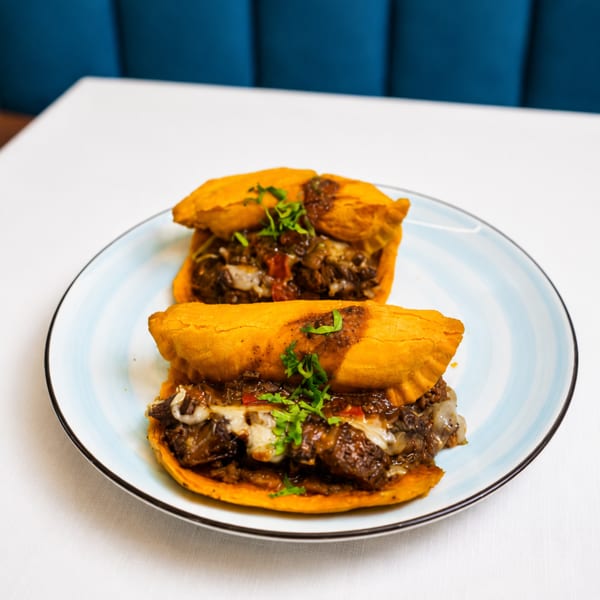 Two golden-brown empanadas filled with savory meat and cheese, garnished with fresh herbs on a light blue plate.
