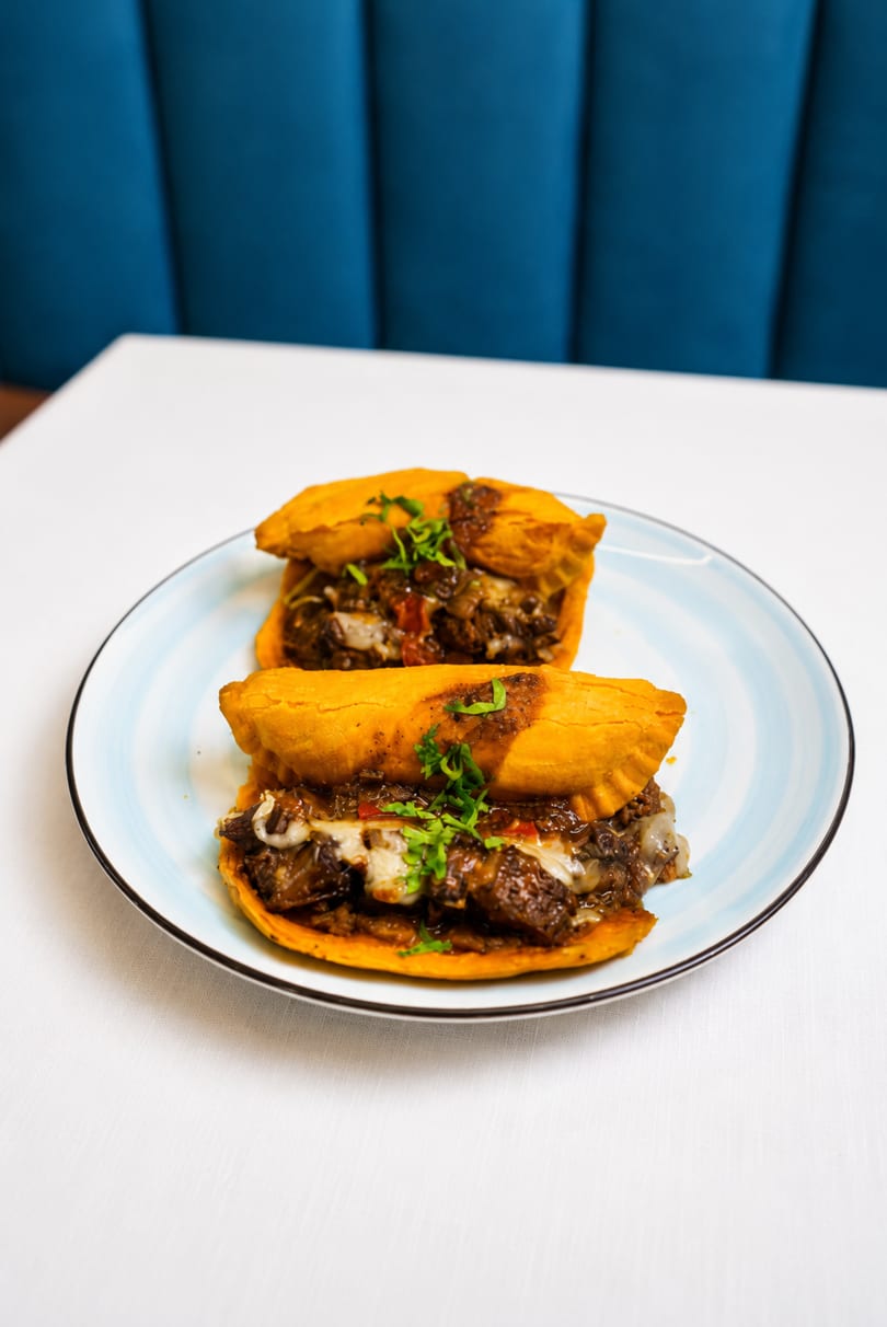 Two golden-brown empanadas filled with savory meat and cheese, garnished with fresh herbs on a light blue plate.