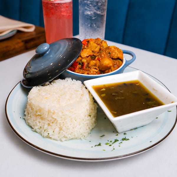 Chicken stew with rice and black bean soup on a white plate with drinks in the background.