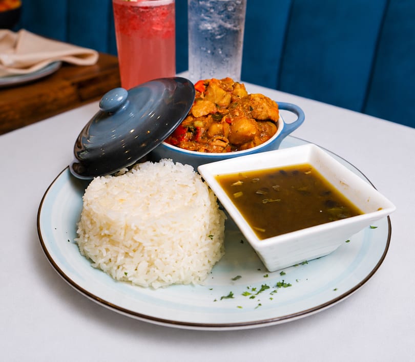 Chicken stew with rice and black bean soup on a white plate with drinks in the background.