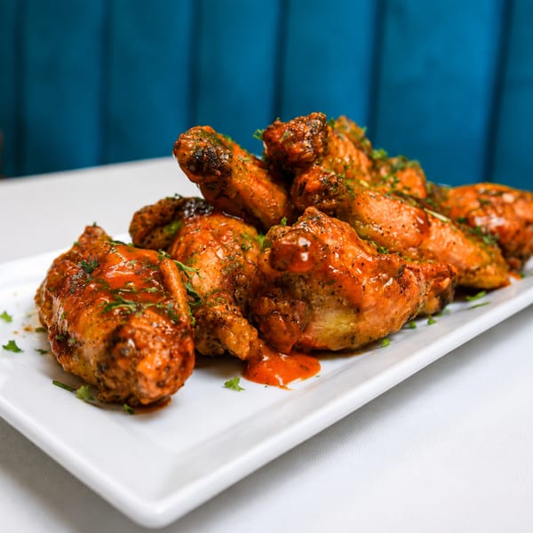 A white rectangular plate piled high with saucy, golden-brown chicken wings, garnished with fresh herbs.