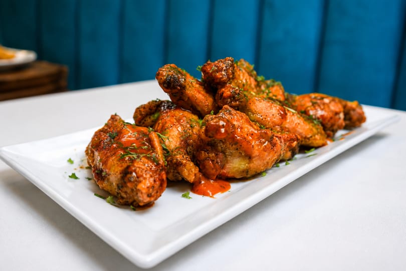 A white rectangular plate piled high with saucy, golden-brown chicken wings, garnished with fresh herbs.