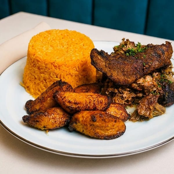 A plate of roasted pork, yellow rice, and fried plantains on a white tablecloth.