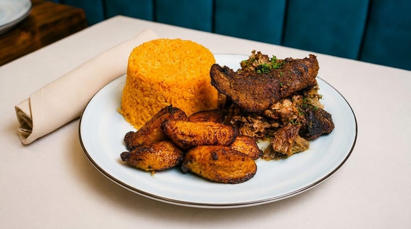 A plate of roasted pork, yellow rice, and fried plantains on a white tablecloth.