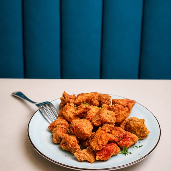 A light blue plate filled with golden-brown fried chicken pieces, garnished with parsley, on a white table.