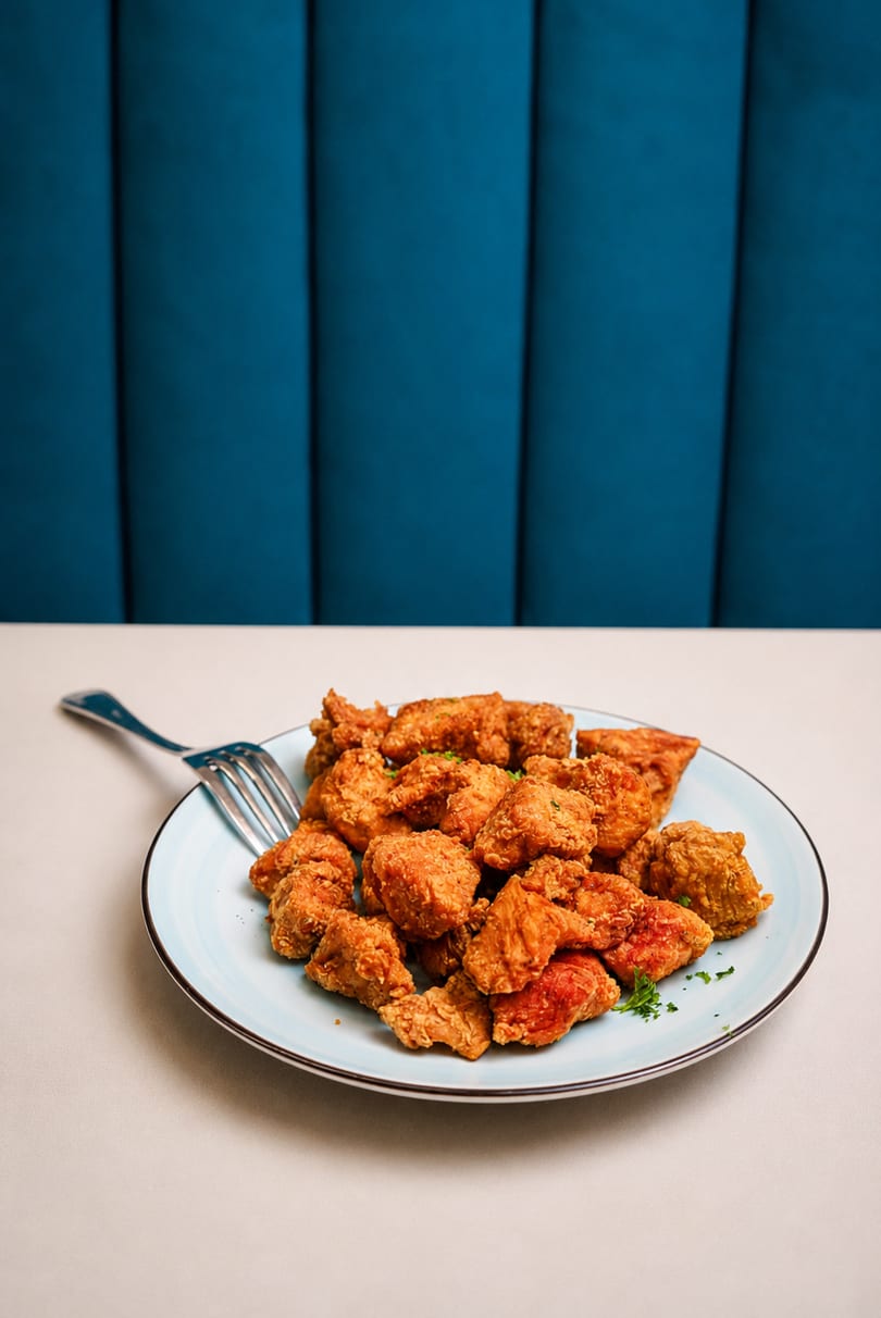 A light blue plate filled with golden-brown fried chicken pieces, garnished with parsley, on a white table.