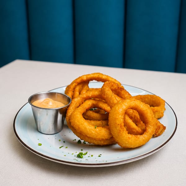 Golden-brown onion rings with a side of dipping sauce on a light blue plate.