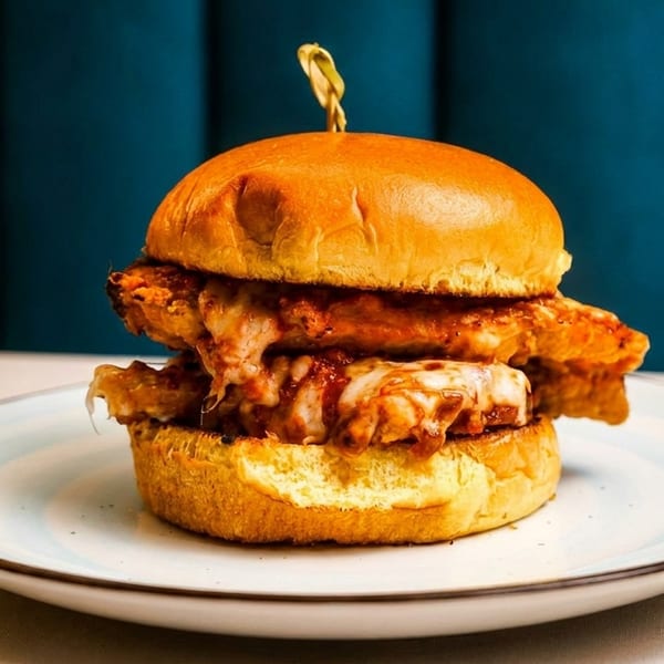 A cheesy chicken sandwich on a brioche bun, served on a white plate with blue accents.