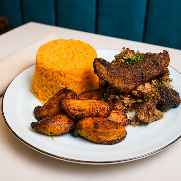 A plate of yellow rice, fried plantains, and shredded meat on a white tablecloth.