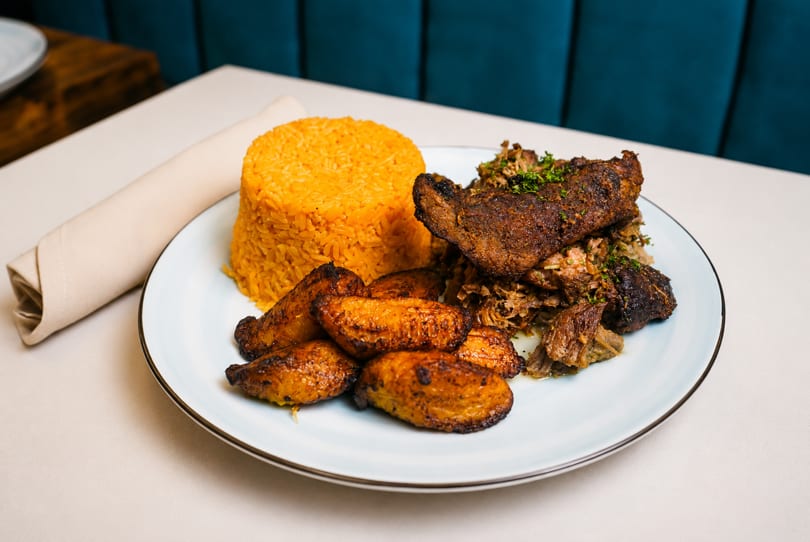 A plate of yellow rice, fried plantains, and shredded meat on a white tablecloth.