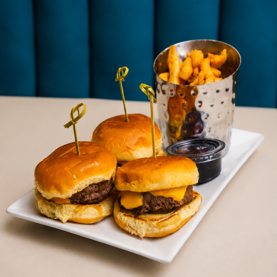Three cheeseburger sliders with toothpicks, a side of fries in a metal cup, and dipping sauce.