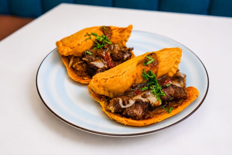 Two golden-fried empanadas, filled with savory meat and cheese, garnished with fresh parsley on a white plate.