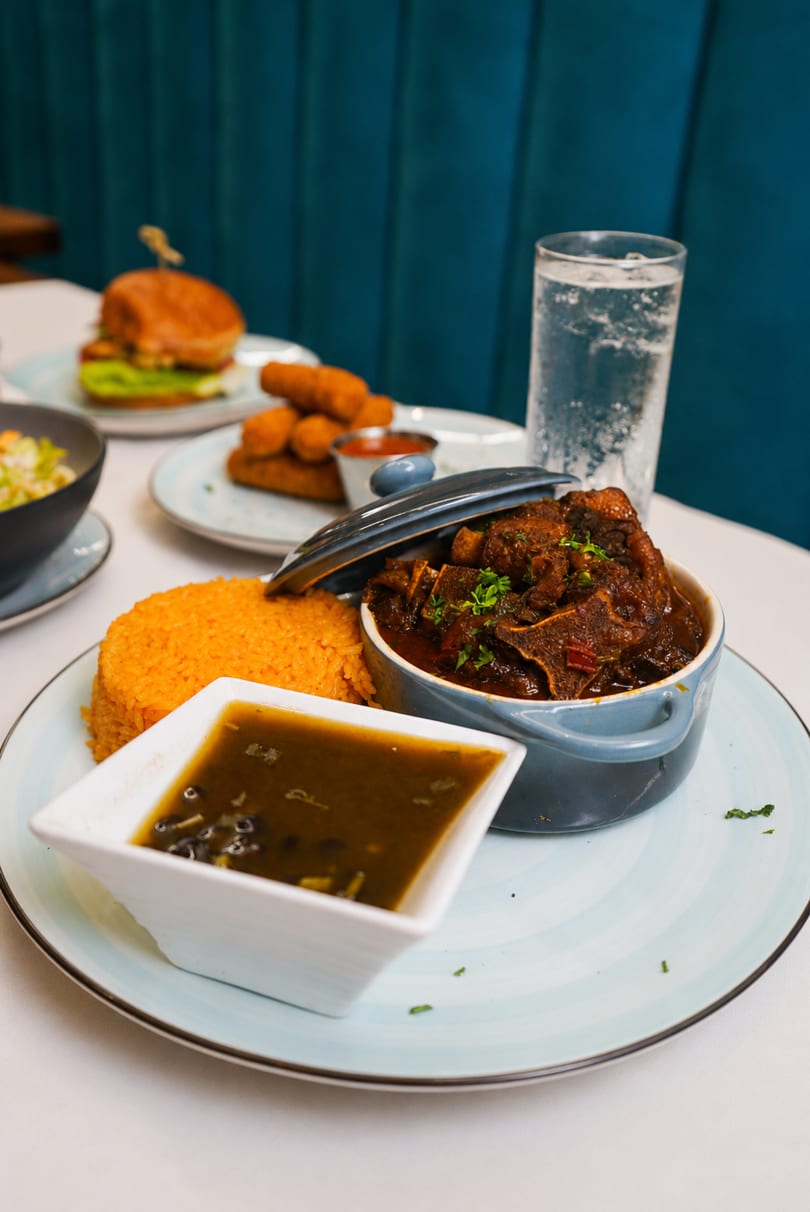 Oxtail stew with rice and black beans, with a burger and mozzarella sticks in the background.