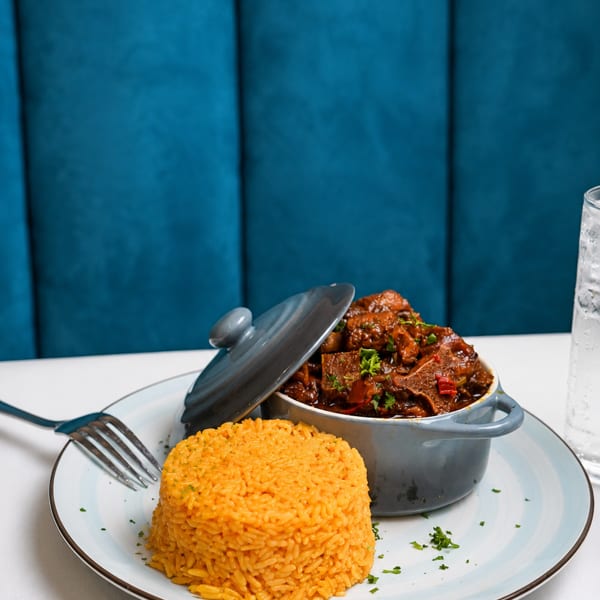 A gray pot of stewed meat and a mound of orange rice on a white and blue plate.