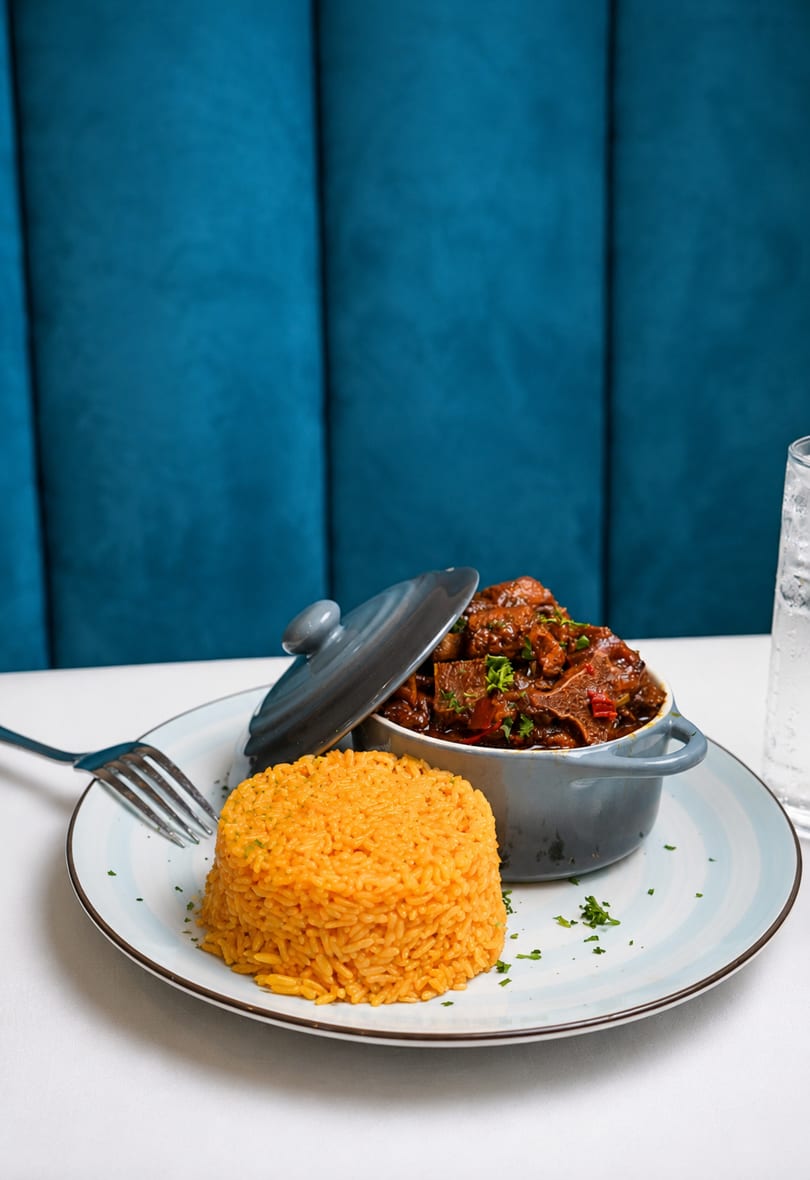 A gray pot of stewed meat and a mound of orange rice on a white and blue plate.