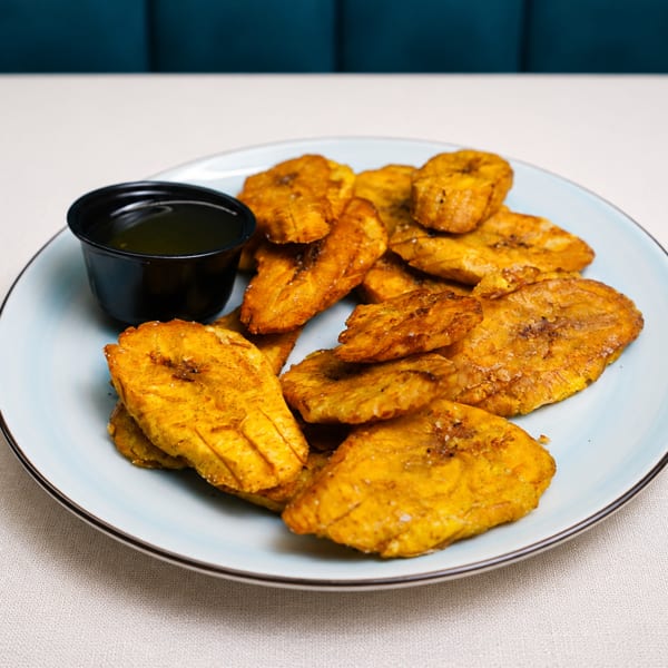 A light blue plate filled with golden-brown fried plantains and a small black cup of dipping sauce.