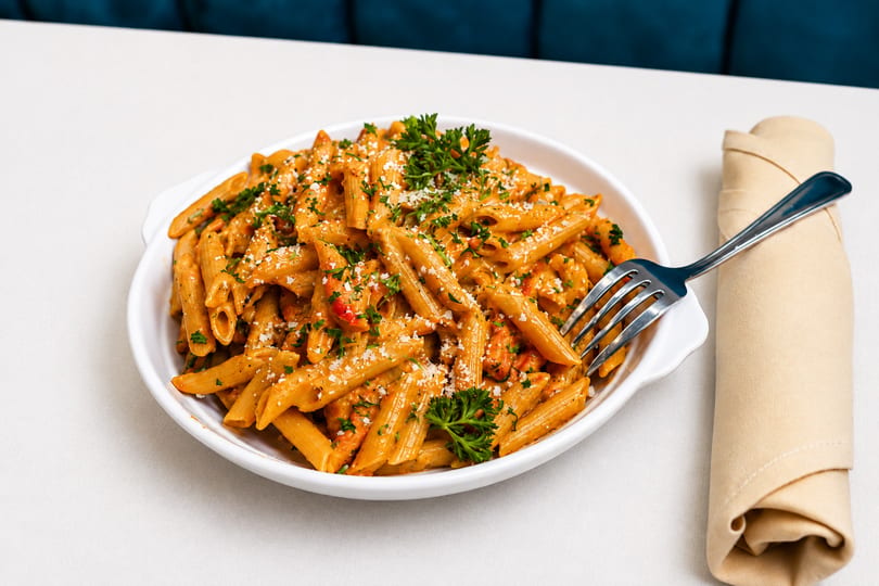 Penne pasta with creamy tomato sauce, shrimp, parsley, and parmesan cheese in a white bowl.