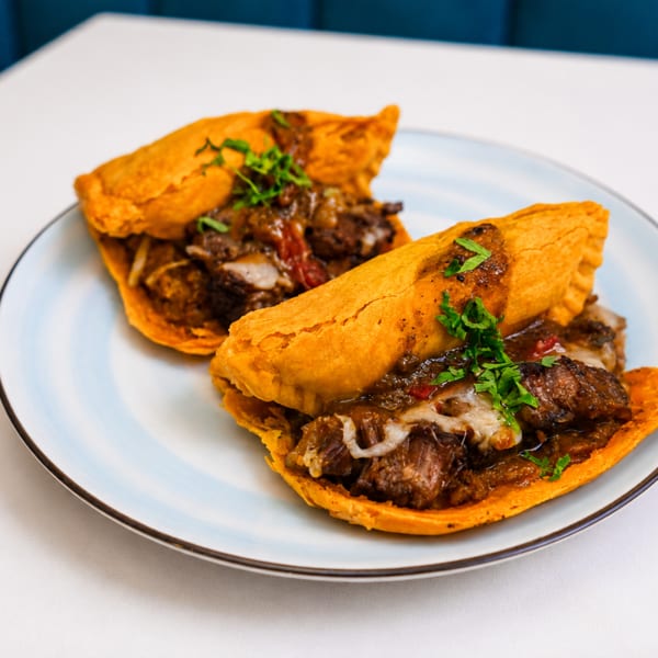 Two golden-fried empanadas filled with savory meat and cheese, garnished with fresh parsley on a plate.